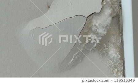 Cracked wall with peeling paint and plaster damage, showing texture and deterioration 139536349