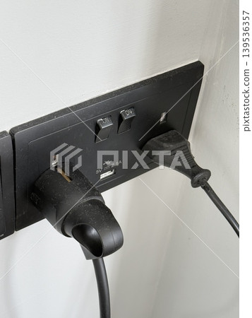 Electrical outlet with two plugged-in cords on a white wall, close-up shot Electrical outlet with two plugged-in cords on a white wall, close-up shot 139536357
