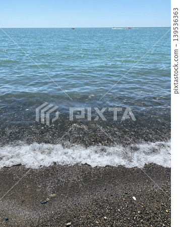 Ocean waves gently lapping onto pebble beach on sunny day, perfect for background use 139536363