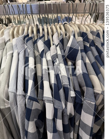 Folded checkered shirts in shades of blue, gray, and white displayed on hangers in a store 139536375