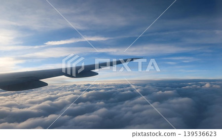 horizontal photo of close up airplane wing extending over thick cloud layer with clear blue sky and sunlight streaks above with copy space 139536623