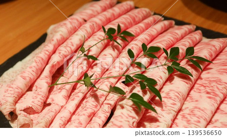 close up of Thinly sliced marbled Wagyu beef arranged in rows on dark plate with garnish sprig for sukiyaki close up of Thinly sliced marbled Wagyu beef arranged in rows on dark plate with garnish sprig for sukiyaki 139536650