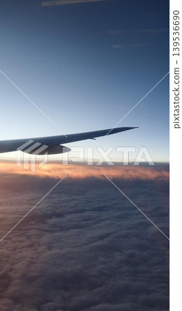 vertical photo of close up airplane wing extending over thick cloud layer with clear blue sky and sunlight streaks below at dawn with copy space vertical photo of close up airplane wing extending over thick cloud layer with clear blue sky and sunlight streaks below at dawn with copy space 139536690