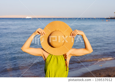 Woman holding straw hat over face on sunny beach Woman holding straw hat over face on sunny beach 139537012