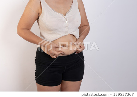 Overweight woman hand pinching excessive belly fat on gray background, Healthy concept Overweight woman hand pinching excessive belly fat on gray background, Healthy concept 139537367