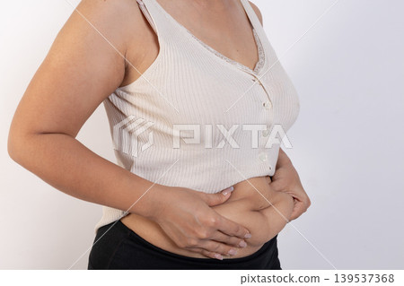 Overweight woman hand pinching excessive belly fat on gray background, Healthy concept Overweight woman hand pinching excessive belly fat on gray background, Healthy concept 139537368