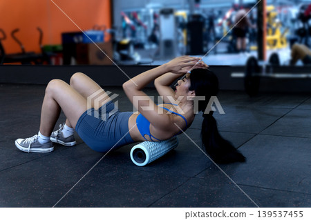 young woman is exercising while lying down using a circular device to roll on the floor 139537455