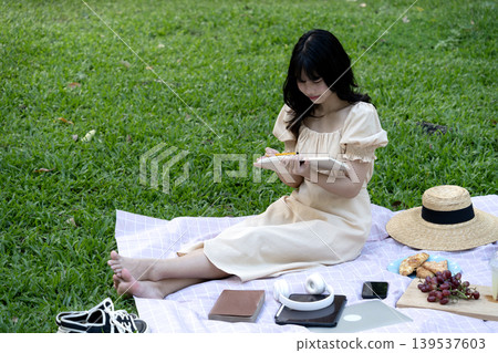 beautiful young woman smiling while sitting in a meadow  enjoying write note 139537603