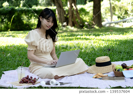 Young woman using laptop while having picnic on mat in park Young woman using laptop while having picnic on mat in park 139537604