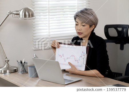 Elder Business woman is sitting at a desk with a laptop and a tablet Elder Business woman is sitting at a desk with a laptop and a tablet 139537779