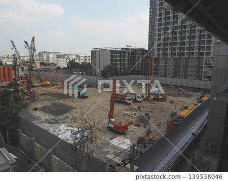 An industrial Bangkok construction site featuring a towering crane against the urban skyline with busy transport roads and concrete building architecture 139538046