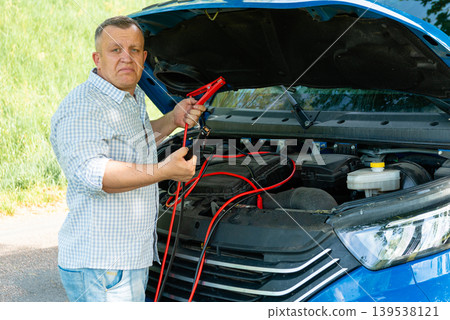 Truck driver holding jumper cables near open hood Truck driver holding jumper cables near open hood 139538121