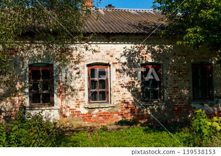 Weathered brick wall of an aged house with three wooden windows, sunlit through green leaves, exuding a time-worn rustic vibe Weathered brick wall of an aged house with three wooden windows, sunlit through green leaves, exuding a time-worn rustic vibe 139538153