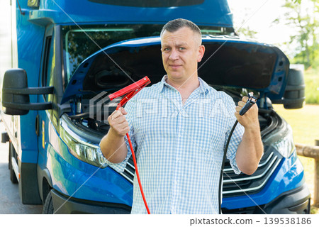 Driver holding jumper cables near truck with open hood Driver holding jumper cables near truck with open hood 139538186