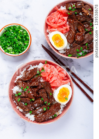 Gyudon Japanese beef with rice, pickled ginger, boiled egg slice, garnished with green onions, in a bowl with chopsticks, Gyudon Japanese beef with rice, pickled ginger, boiled egg slice, garnished with green onions, in a bowl with chopsticks, 139538678