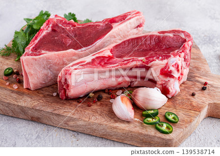 Fresh pieces of beef on the bone, on a wooden cutting board, with herbs and spices, ready for cooking in the kitchen Fresh pieces of beef on the bone, on a wooden cutting board, with herbs and spices, ready for cooking in the kitchen 139538714