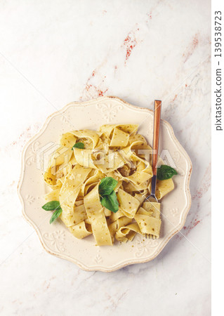 Fresh papardelle pasta, with basil and pesto sauce, is served, on a white plate, with a fork held by hand Fresh papardelle pasta, with basil and pesto sauce, is served, on a white plate, with a fork held by hand 139538723