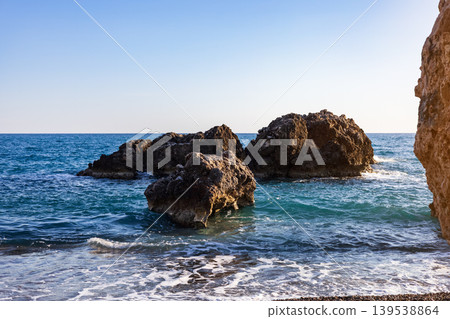 Large rugged rocks in blue water at sunny beach Large rugged rocks in blue water at sunny beach 139538864