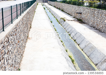 Narrow concrete water canal with stone retaining walls Narrow concrete water canal with stone retaining walls 139538893