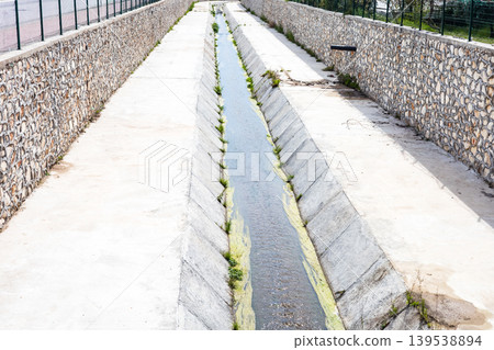 Concrete drainage channel with stone walls in rural setting Concrete drainage channel with stone walls in rural setting 139538894