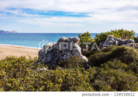 Large stone formation overlooking a blue sea and sandy beach Large stone formation overlooking a blue sea and sandy beach 139538912