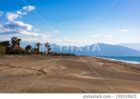 Sandy beach with palm trees and distant blue mountains Sandy beach with palm trees and distant blue mountains 139538925