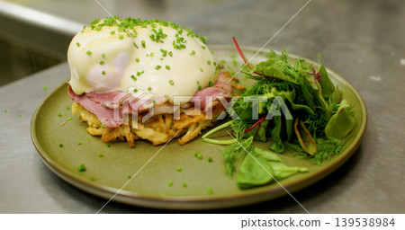 Egg benedict. Brunch meal. Professional dish gastronomy green garnished salad with ham hollandaise sauce on plate in restaurant. Egg benedict. Brunch meal. Professional dish gastronomy green garnished salad with ham hollandaise sauce on plate in restaurant. 139538984