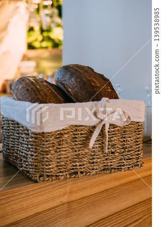 Fresh bread. Sourdough loaf. Rustic food in wicker basket lined with white cloth on wooden counter. Bakery product with brown crust. Fresh bread. Sourdough loaf. Rustic food in wicker basket lined with white cloth on wooden counter. Bakery product with brown crust. 139538985