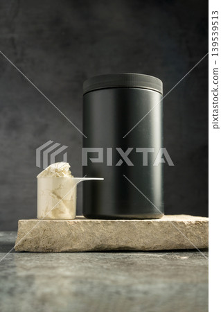 Protein whey powder black plastic tube, on dark background with scoop. Protein whey powder black plastic tube, on dark background with scoop. 139539513
