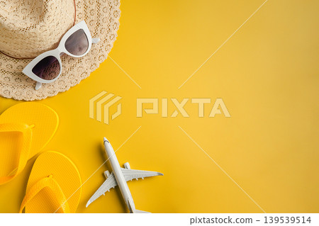 Travel-themed flat lay, summer holiday background. Toy model airplane, sunglasses, sun hat over yellow backgrounds, copy space 139539514