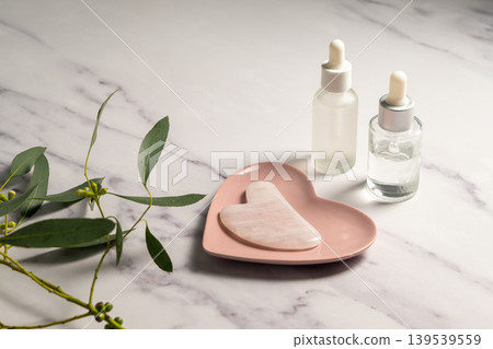 Rose quartz gua sha tool and oil bottles, face massage tool, beauty abstract photo Rose quartz gua sha tool and oil bottles, face massage tool, beauty abstract photo 139539559