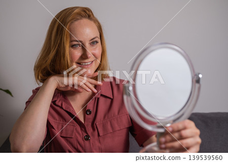 Smiling, happy middle age woman looking at mirror touching her skin, aging, skin care 139539560