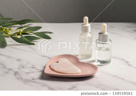 Rose quartz gua sha tool and oil bottles, face massage tool, beauty abstract photo Rose quartz gua sha tool and oil bottles, face massage tool, beauty abstract photo 139539561