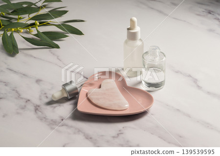 Rose quartz gua sha tool and oil bottles, face massage tool, beauty abstract photo Rose quartz gua sha tool and oil bottles, face massage tool, beauty abstract photo 139539595