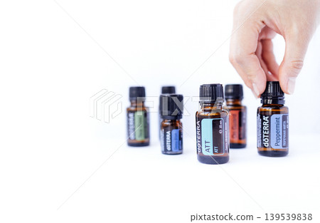 Hand reaching for essential oil bottle among various amber glass containers, showcasing natural wellness products with vibrant labels and a clean, minimalist background Hand reaching for essential oil bottle among various amber glass containers, showcasing natural wellness products with vibrant labels and a clean, minimalist background 139539838