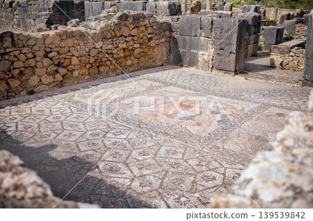 Ancient mosaic floor with intricate geometric patterns and vibrant colors, surrounded by stone ruins, showcasing historical craftsmanship and archaeological significance Ancient mosaic floor with intricate geometric patterns and vibrant colors, surrounded by stone ruins, showcasing historical craftsmanship and archaeological significance 139539842