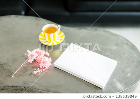 White notebook placed on a modern coffee table with a cup of tea and pink flowers, creating a serene and inviting atmosphere for relaxation and creativity 139539849