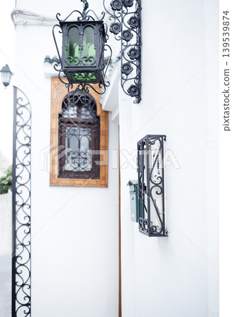 Elegant street scene featuring a vintage lantern and decorative wrought iron details against a pristine white wall, showcasing architectural beauty and charm in a tranquil setting Elegant street scene featuring a vintage lantern and decorative wrought iron details against a pristine white wall, showcasing architectural beauty and charm in a tranquil setting 139539874