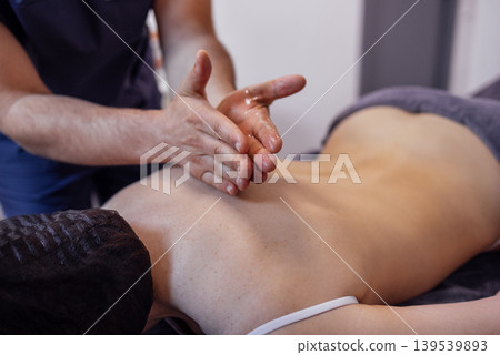 Massage therapist gives a back massage to his female client in a spa salon or clinic. 139539893