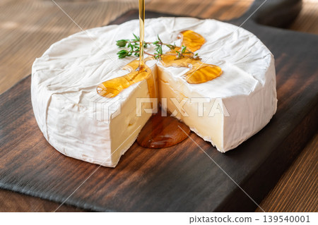 Golden Maple Syrup Pouring Over Camembert Cheese On Rustic Wooden Board Elegantly Golden Maple Syrup Pouring Over Camembert Cheese On Rustic Wooden Board Elegantly 139540001