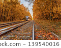 Tram travels along railway tracks through autumn forest with fallen leaves and golden foliage on both sides. Concept of journey, seasonal transport, travel route, nature connection, leaf fall, fall 139540016