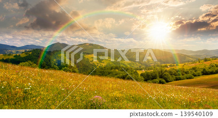 sunset over mountainous countryside landscape in summer. grassy field on a hillside. view of a forested mountain ridge in the distance. wonderful weather with cloudy sky and rainbow 139540109