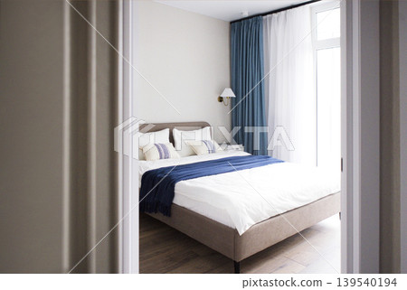 Modern bedroom interior featuring a neatly made bed with white linens and blue throw blanket, large windows with sheer curtains, and wooden flooring visible through an open door Modern bedroom interior featuring a neatly made bed with white linens and blue throw blanket, large windows with sheer curtains, and wooden flooring visible through an open door 139540194