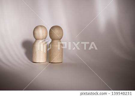 Two wooden figurines standing side by side on a smooth surface with soft lighting creating gentle shadows in the background 139540231