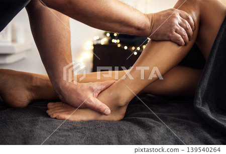 Male massage therapist providing a relaxing leg massage to a female client on a soft towel-covered table in a serene spa environment with warm lighting and soothing ambiance Male massage therapist providing a relaxing leg massage to a female client on a soft towel-covered table in a serene spa environment with warm lighting and soothing ambiance 139540264