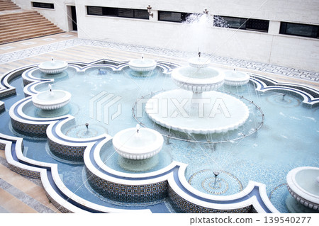 Ornate fountain with multiple tiers and intricate tile patterns, surrounded by tranquil water, creating a serene atmosphere in a beautifully designed courtyard space Ornate fountain with multiple tiers and intricate tile patterns, surrounded by tranquil water, creating a serene atmosphere in a beautifully designed courtyard space 139540277