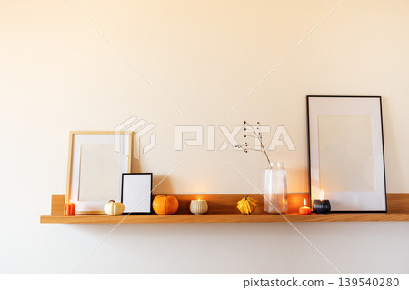 Minimalist shelf display featuring empty frames, decorative pumpkins, and candles, creating a warm and inviting atmosphere for seasonal home decor inspiration Minimalist shelf display featuring empty frames, decorative pumpkins, and candles, creating a warm and inviting atmosphere for seasonal home decor inspiration 139540280