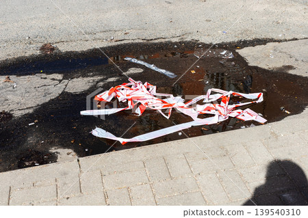 Wet pavement with caution tape. Postincident urban scene with spilled paint and shadows Wet pavement with caution tape. Postincident urban scene with spilled paint and shadows 139540310