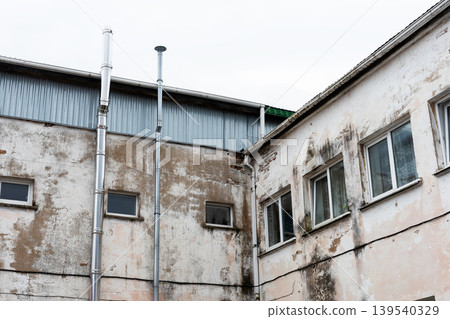 Abandoned factory with weathered exterior. Dilapidated industrial structure under gloomy sky Abandoned factory with weathered exterior. Dilapidated industrial structure under gloomy sky 139540329