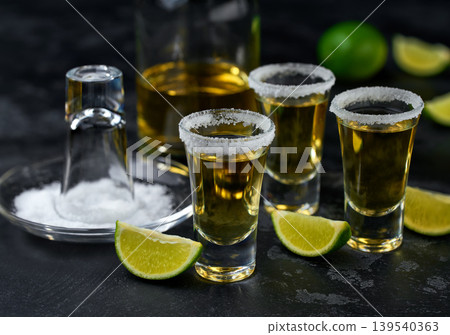 Golden tequila glasess shots with lime slices and salt crystals on a dark table, selective focus. 139540363
